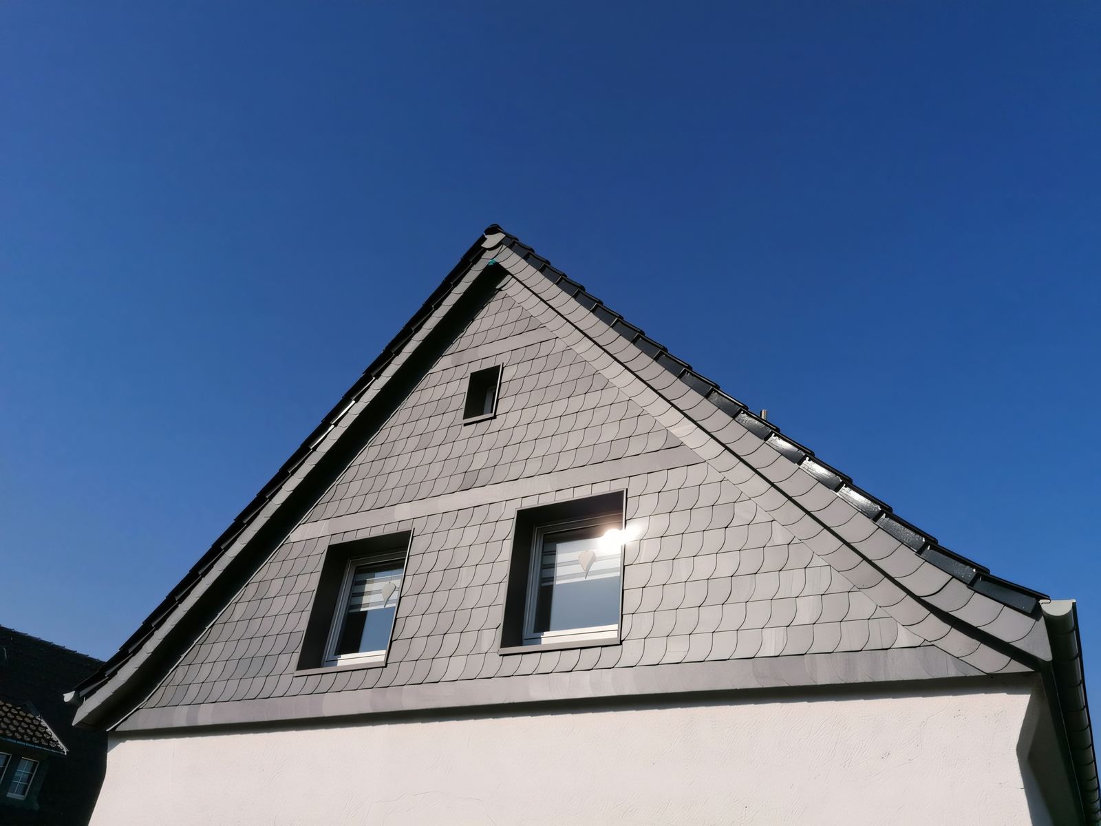 Giebeldreieck mit Schieferbekleidung in Schuppenform und zwei Fenstern, darunter weißer Putz