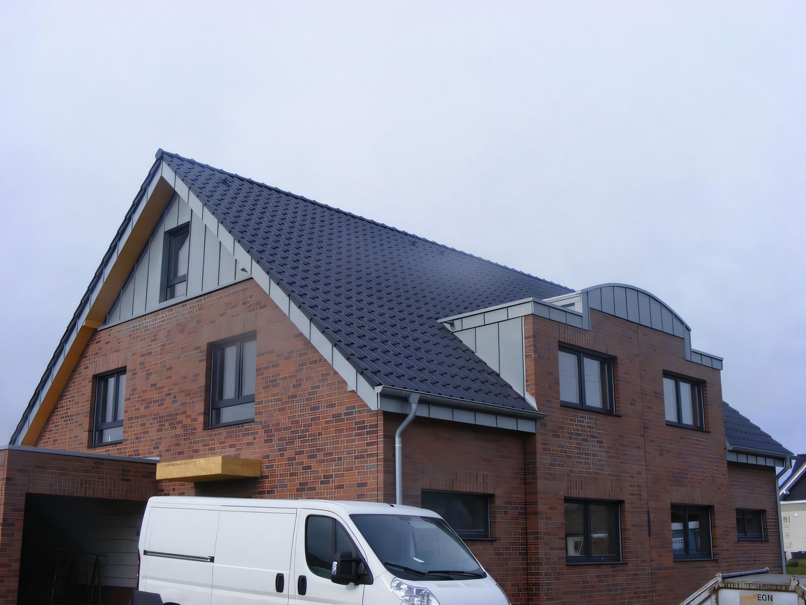 Neubau aus rotem Klinker mit anthrazitfarbenem Ziegeldach, Giebel mit senkrechter grauer Metallbekleidung und Metallgaube mit Tonnendach