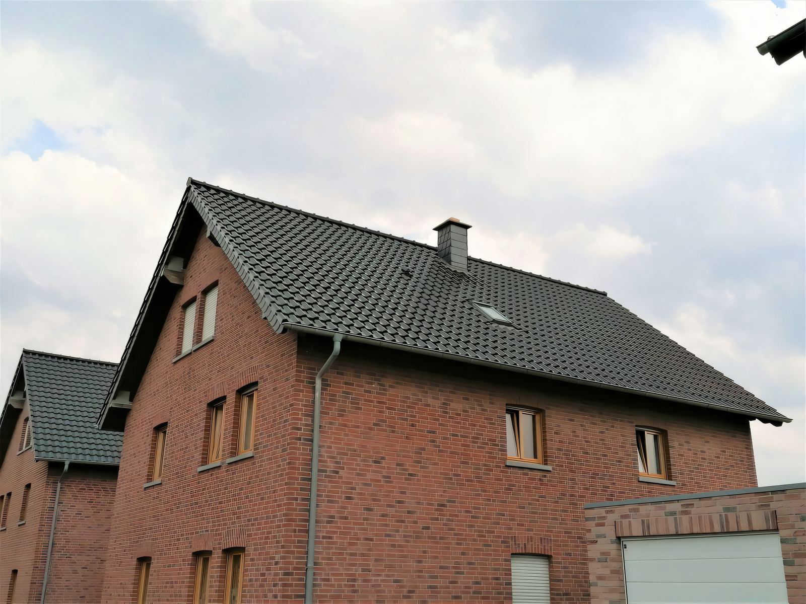 Klinker-Mehrfamilienhaus mit anthrazitfarbenem Ziegeldach und Schornstein, von schräg unten fotografiert