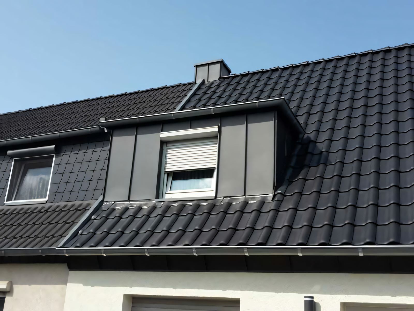 Gaube mit anthrazitfarbener senkrechter Metallbekleidung und Rollladen auf einem dunklen Ziegeldach