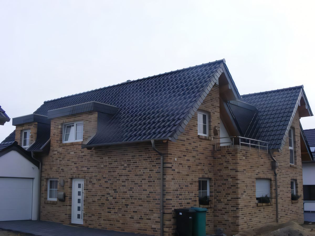 Klinkerhaus mit dunklem Ziegeldach, Gaube und mehreren Giebeln, links die Garage