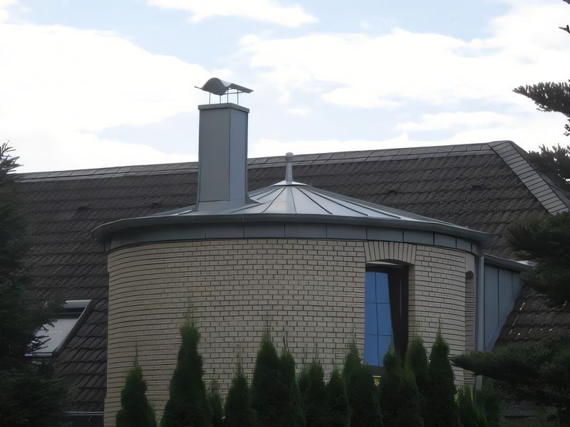 Runder Treppenturm mit Kegeldach in Metall, dahinter Schornstein und Ziegeldach