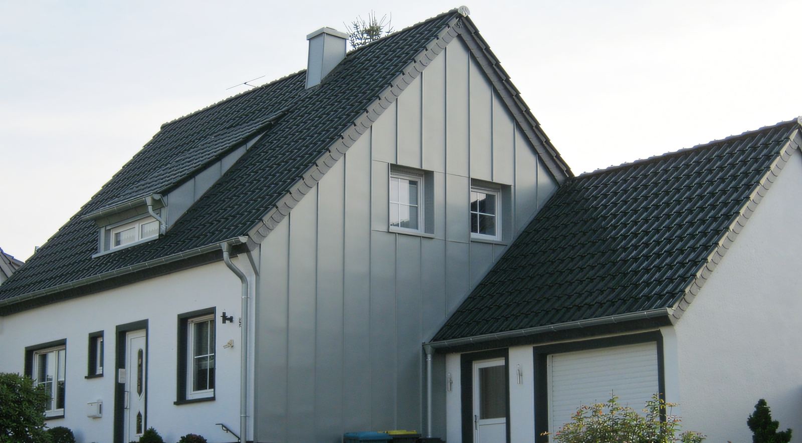 Einfamilienhaus mit grauer Stehfalzbekleidung am Giebel und dunklem Ziegeldach