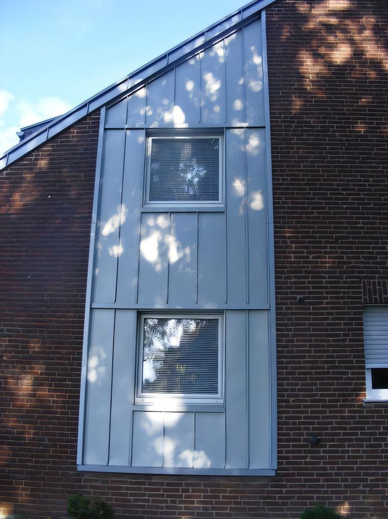 Senkrechtes Fensterband mit hellgrauer Metall-Stehfalzbekleidung in einer Klinkerwand