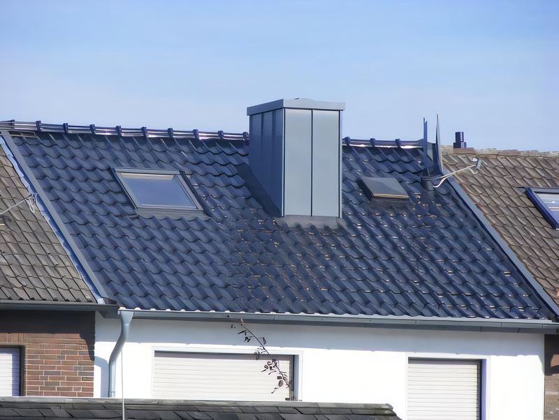 Blauschwarzes Ziegeldach mit metallbekleidetem Schornstein und zwei Dachfenstern