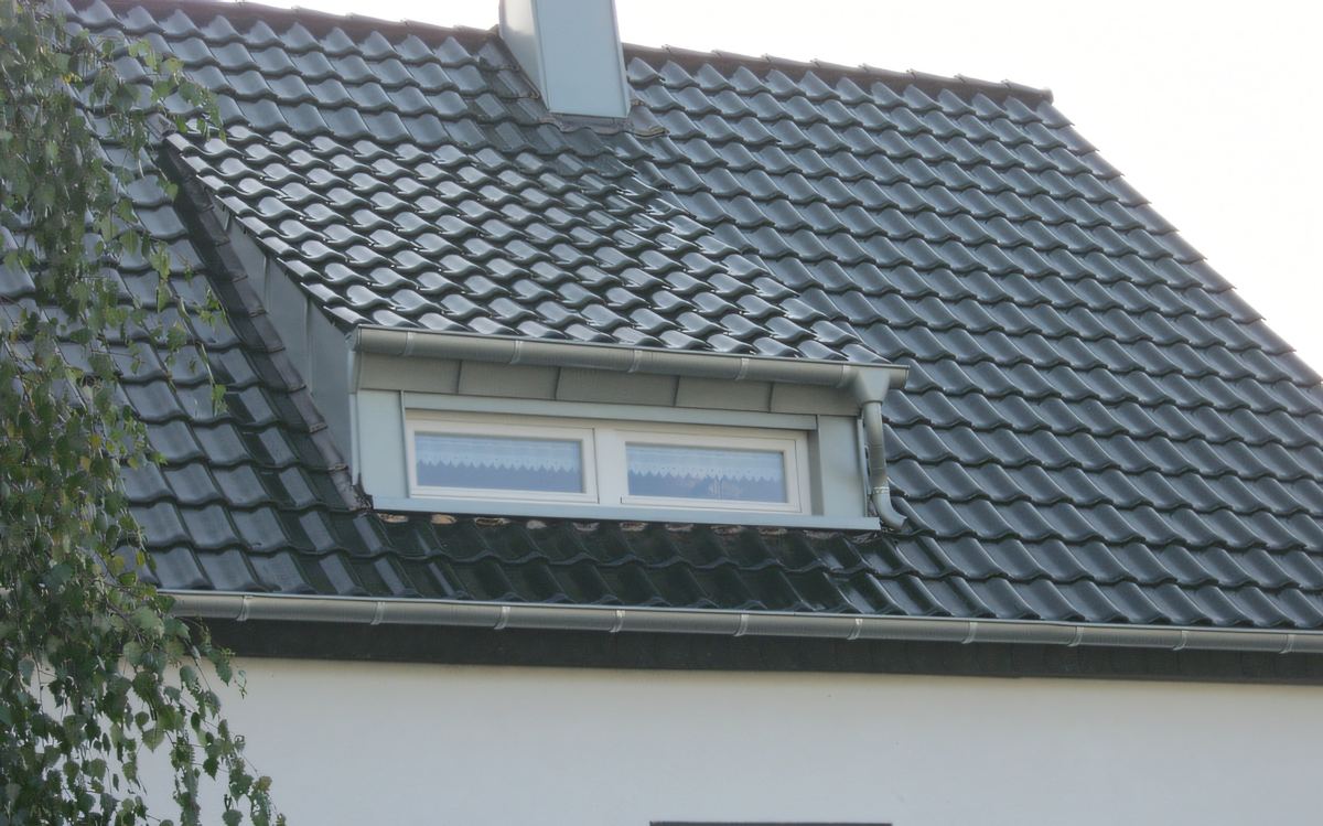 Graues Ziegeldach mit breiter Gaube über einem weißen Haus mit dunklen Fensterrahmen