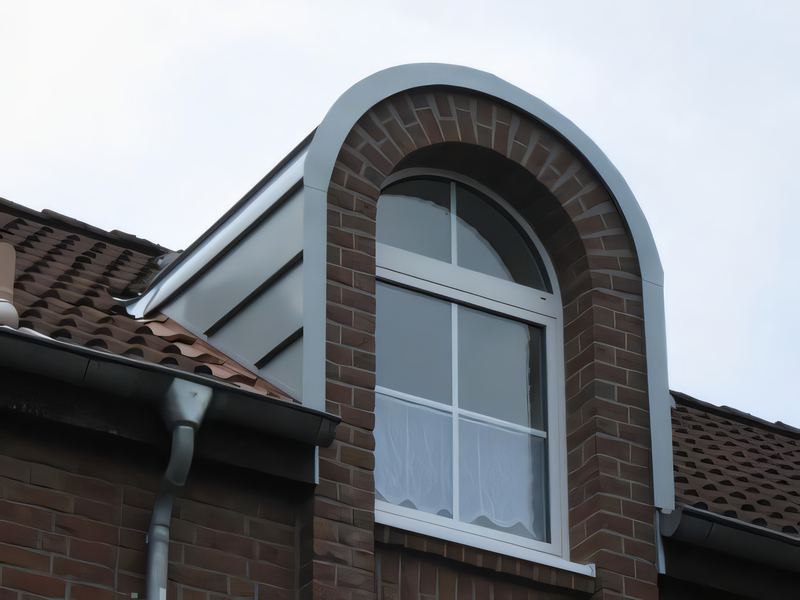 Rundbogengaube mit grauer Metallbekleidung und Klinkerbogen auf einem roten Ziegeldach