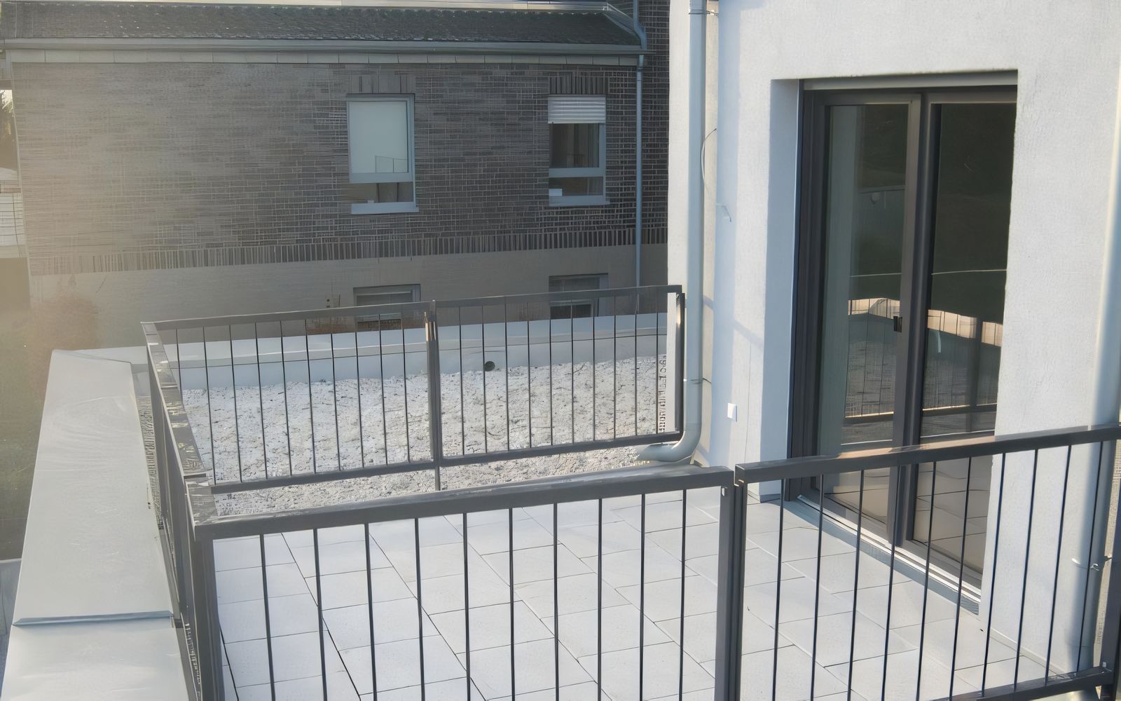 Dachterrasse mit hellen Großformatplatten, Kiesrand und dunklem Stabgeländer vor einem weiß verputzten Haus